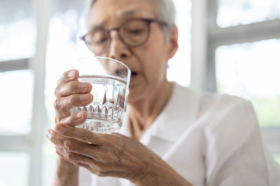 Elderly woman struggling to drink a glass of water due to shaking hands