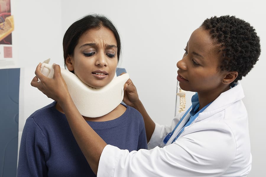Doctor puts a neck brace on her patient who is grimacing in pain