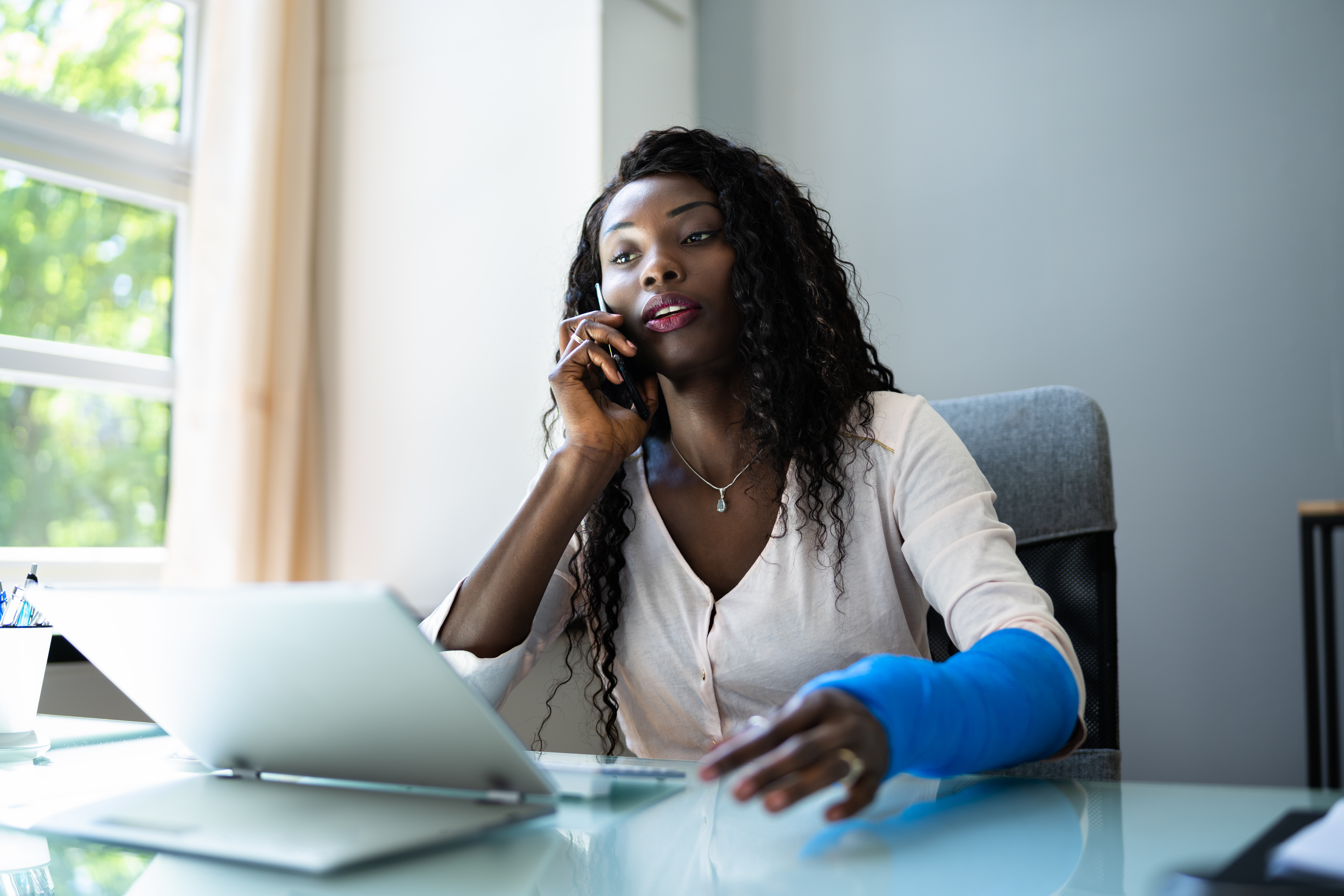 Woman with her arm in a cast sitting in front of her laptop talking to a personal injury lawyer on the phone